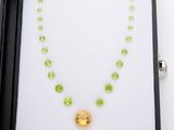 une photo d'un collier orné de pierres vertes et jaunes, présenté dans un écrin