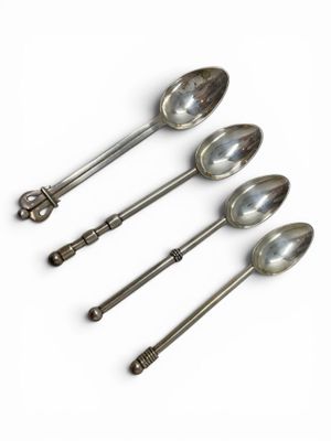 four silver spoons are lined up in a row on a white surface