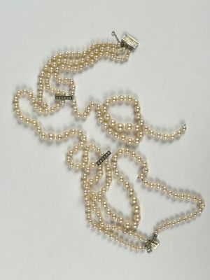 un collier de perles blanches muni d'un fermoir en argent, posé sur un fond blanc