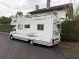 un petit camping-car blanc garé devant une maison