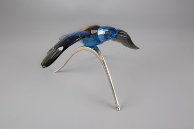 oiseau en verre argenté et bleu perché sur une branche, sur fond gris