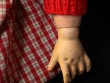 a close up of a doll ' s hand with a red and white checkered shirt