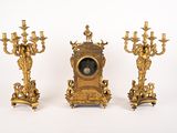 three golden candlesticks and a clock on a white background