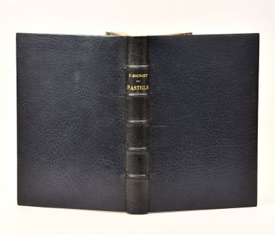 an old book with a black cover sitting on top of a white table