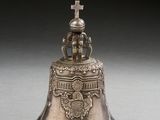 an old silver bell with a cross on top sitting on a table