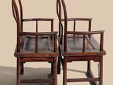 pair of antique chinese chairs with wooden arms and back rests against a beige background