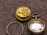 a close up of a gold pocket watch and a ring on a brown surface