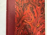 un livre orange et noir avec une couverture rouge posée sur une surface blanche