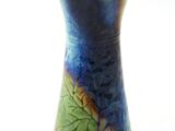 un vase bleu et vert posé sur une surface blanche