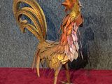 une sculpture représentant un coq, exposée sur un socle rouge
