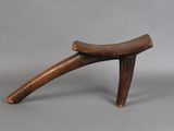 a small wooden stool with a curved seat on a gray surface