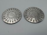 deux pièces d'argent ornées de motifs, posées sur une surface blanche