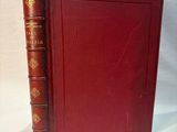 an old book with a red cover sitting on top of a white table