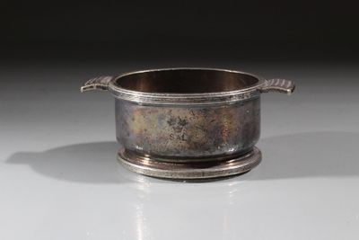 une tasse en argent avec une anse, posée sur une table blanche