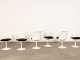 four white tulip chairs with black cushions in a white room