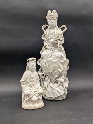 une statue blanche représentant une femme assise sur un rocher, à côté d'une autre statue représentant une femme