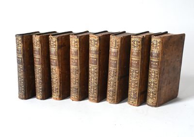 six old books are lined up in a row on a white surface