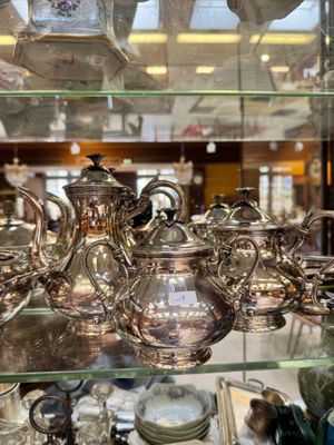 a glass display case filled with silver teapots and other items