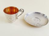 a silver cup and saucer sitting next to each other