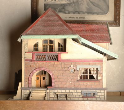 une petite maison de poupées posée sur une étagère, à côté d'une photo encadrée