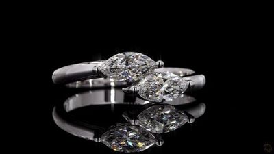 two diamond engagement rings on a reflective surface with a black background