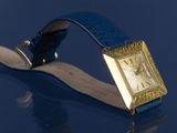 a gold watch on a blue leather strap on a table