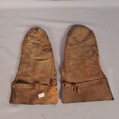 une paire de mitaines en cuir marron, avec leurs étiquettes, posées sur une surface blanche