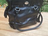 black leather purse on wooden table with stone wall in background