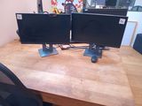 two monitors sitting on a wooden desk with a black chair