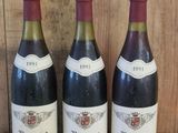 trois bouteilles de vin sont alignées sur une étagère en bois