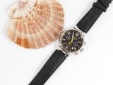 black leather watch strap with a black watch face and a seashell on a white background