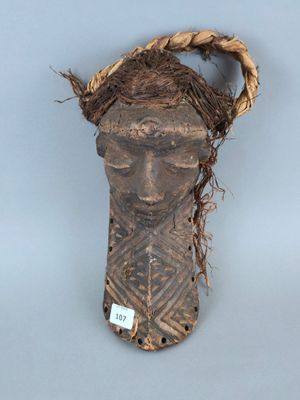 un vieux masque en bois orné d'un bandeau tressé, posé sur une surface grise