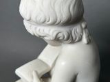 a statue of a boy reading a book on a table