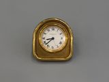 une horloge dorée posée sur un fond gris, avec un cadran blanc