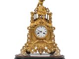 une horloge dorée posée sur un socle, sur fond blanc
