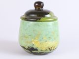 a green and gold jar with a lid on a white surface