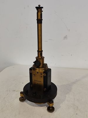 une horloge ancienne en laiton et noir, posée sur un socle, sur une surface blanche