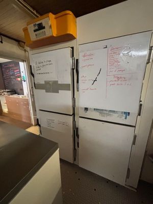 deux réfrigérateurs dans une cuisine où est accroché un tableau blanc au mur