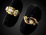 two gold rings with diamonds and a pearl on a black velvet ring holder