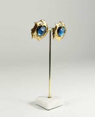 une paire de boucles d'oreilles en or et pierres bleues, présentées sur un présentoir