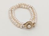 un gros plan sur un bracelet de perles blanches muni d'un fermoir en or