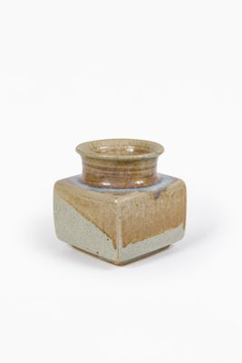 un petit vase marron et blanc posé sur une surface blanche