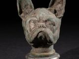 sculpture représentant une tête de chien sur un socle, sur fond noir