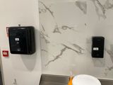 a toilet in a public restroom with a paper towel dispenser on the wall