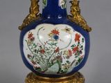 a blue vase that has a gold base and a flower design on it