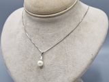 un gros plan d'un collier porté par un mannequin, orné d'une perle blanche
