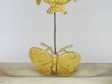 a gold clock on a stand with a butterfly on top of it