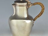 a silver pitcher with a rope handle on a table