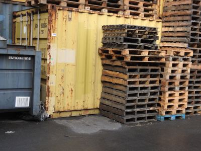 a large stack of pallets in front of a yellow building