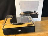 une boîte ouverte contenant un tourne-disque et d'autres appareils électroniques, posée sur une table en bois